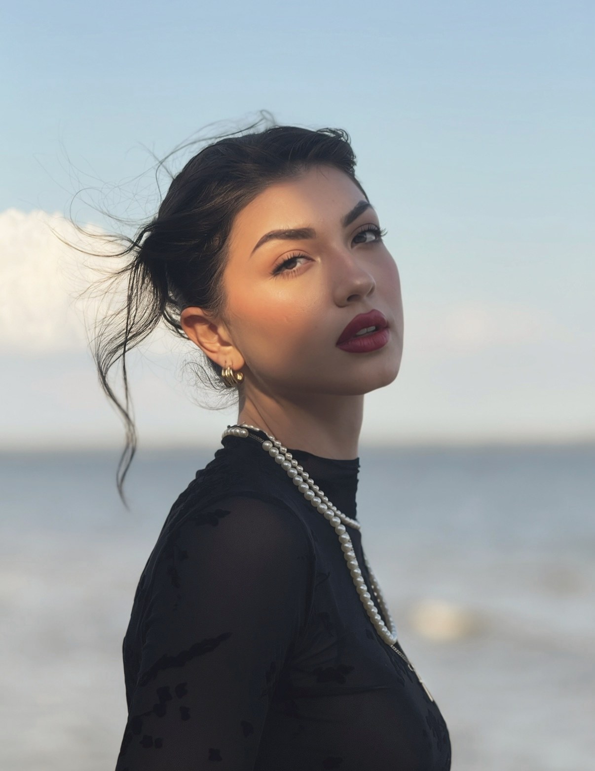 Portrait of Julia Paris-Gainey by the water, in a black dress and pearl necklace