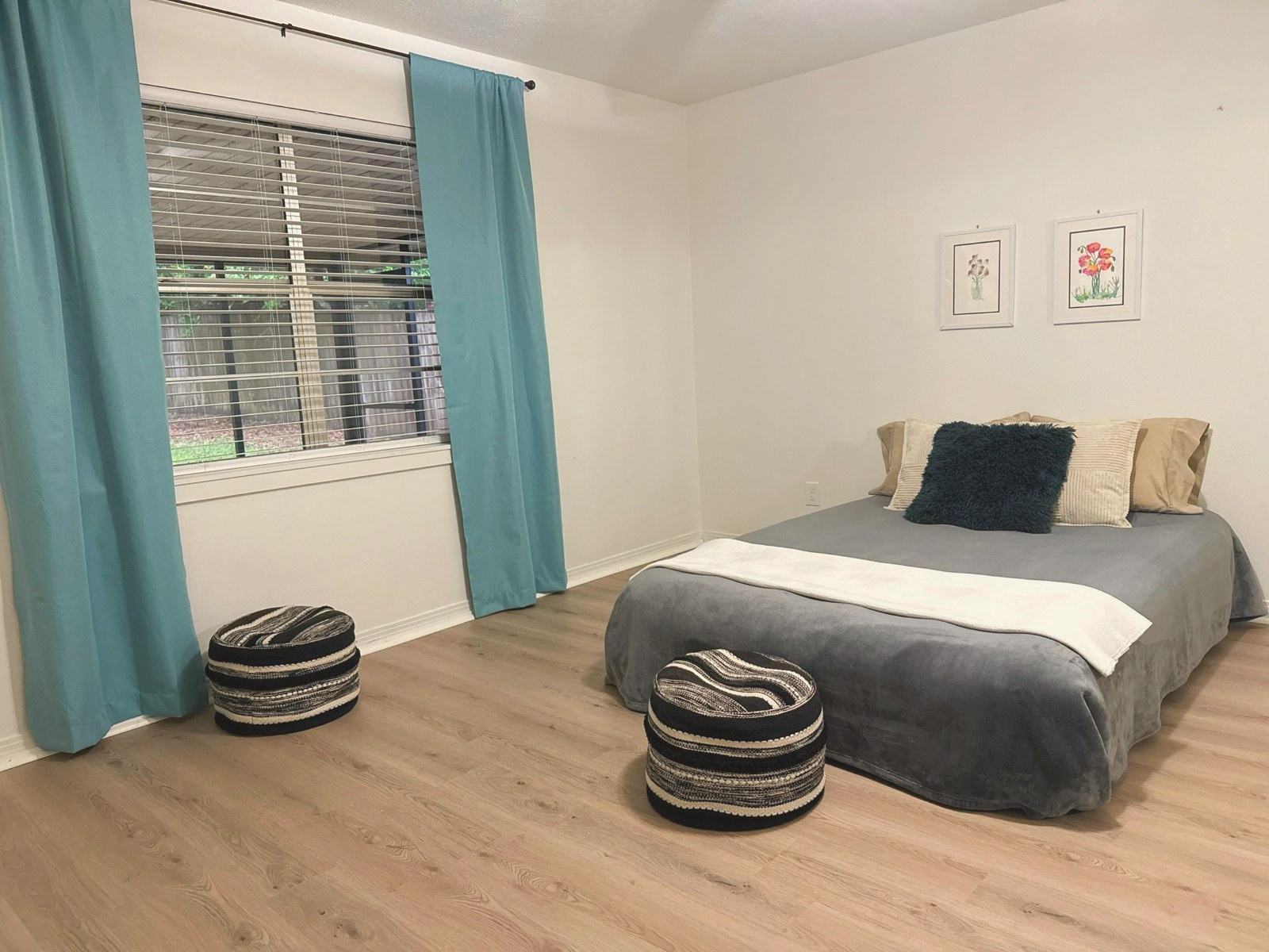 Bedroom with teal curtains, a gray bed, and two woven ottomans