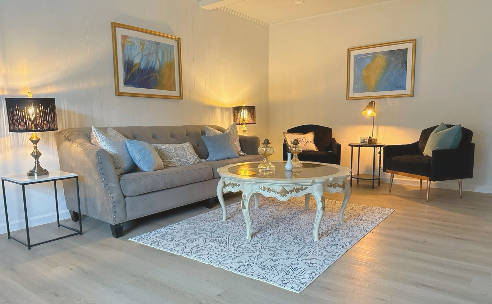 Staged living room with a gray sofa, carved coffee table, and gold-framed art